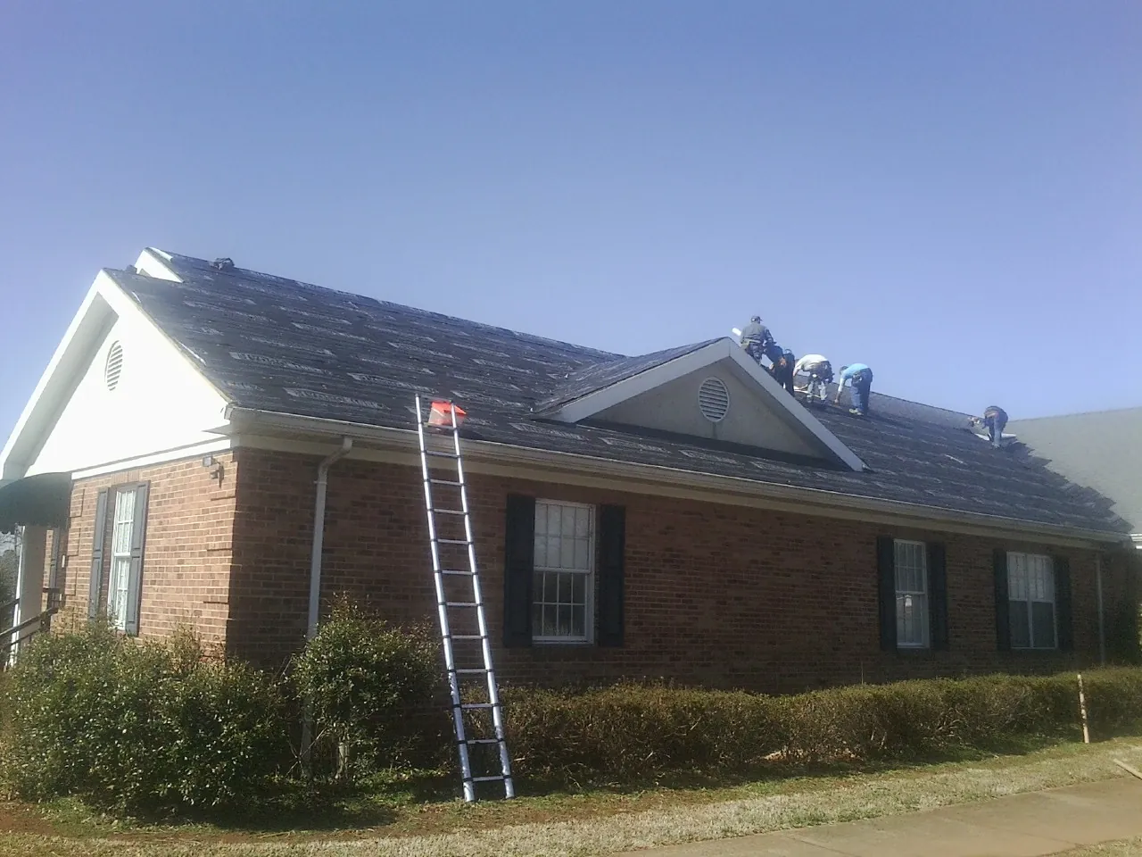 Crew tearing shingles off a brick ranch roof with a ladder set — Emergency Roof Repair work by our crew in Van Nuys