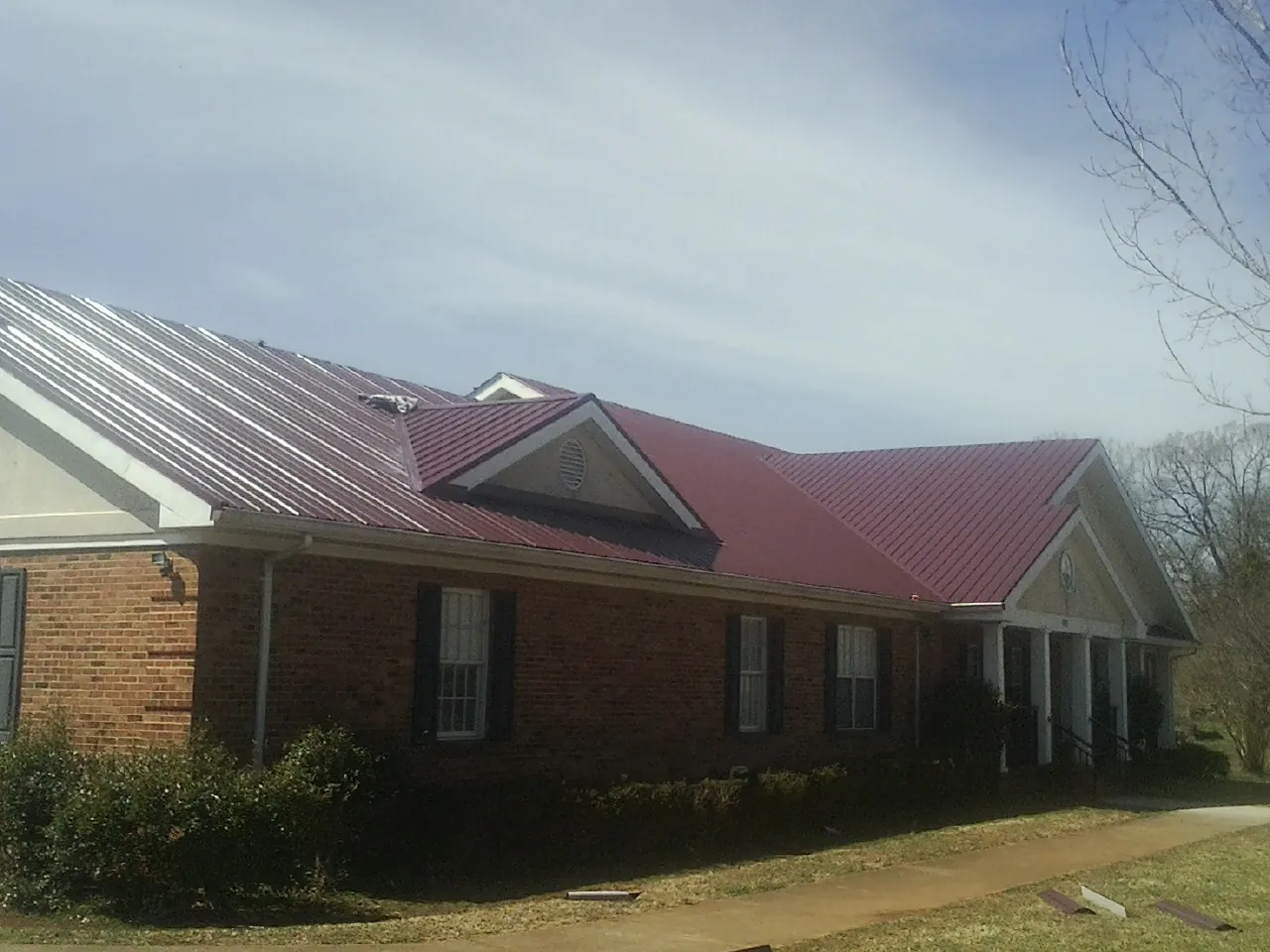 Red metal roof with gabled entries on a long brick building, from a Hail Damage Roof Repair job in Van Nuys