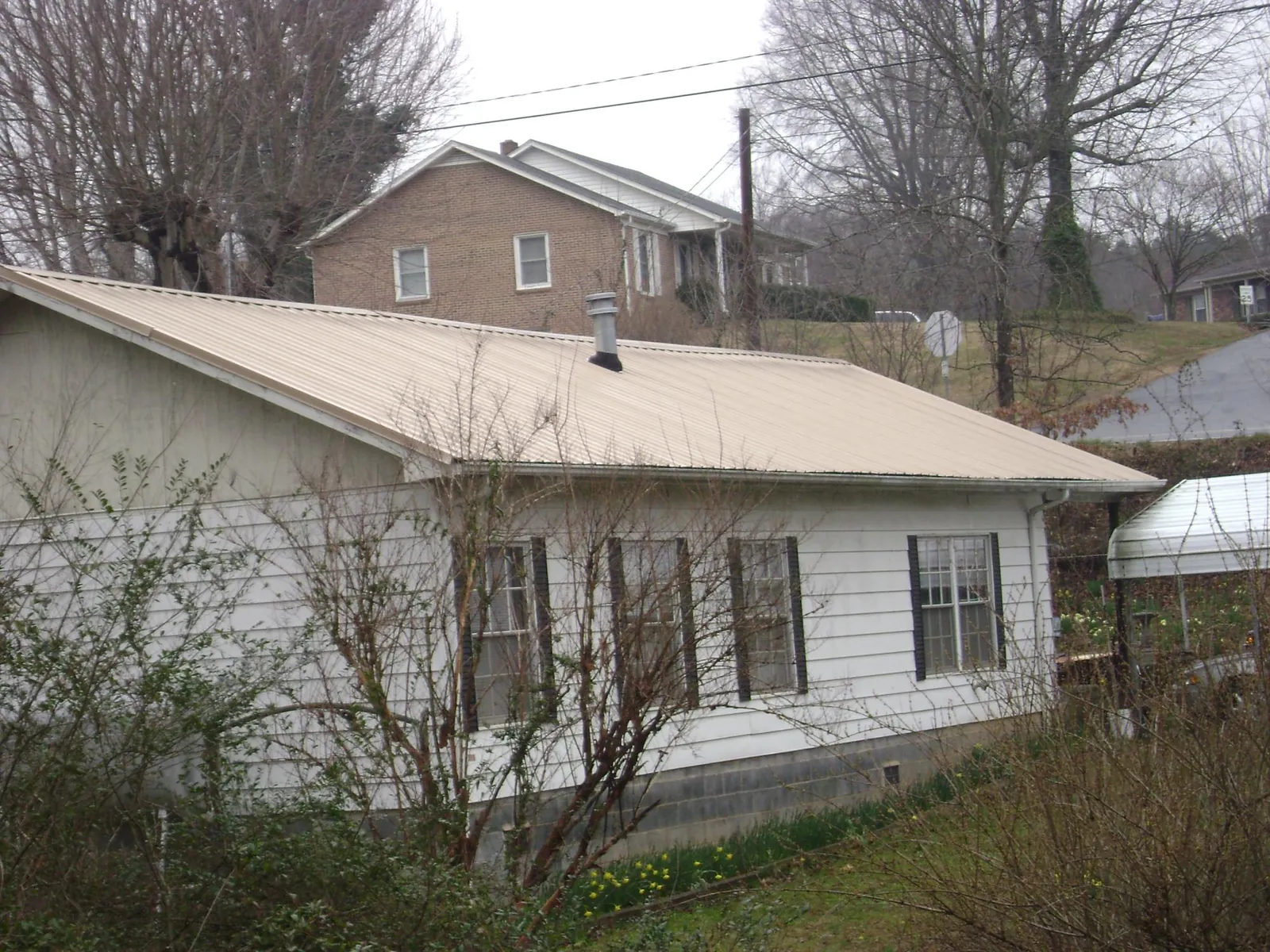 Tan metal roof on a white sided house set into a hillside — Commercial Roofing by Roofing Brothers in Van Nuys